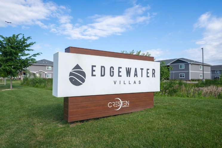 A large sign on grass reads "Edgewater Villas" with a logo and "Cresjen" at the bottom. Residential buildings are visible in the background.